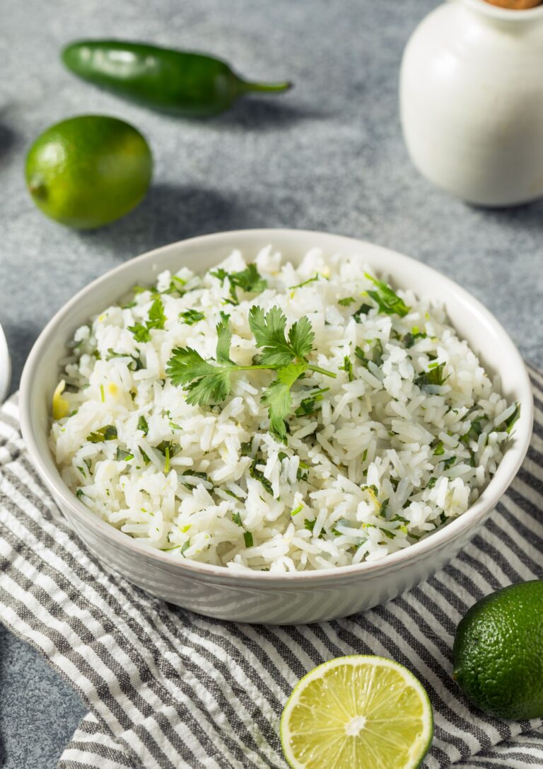 Bowl of cilantro lime rice with lime wedges and cilantro sprigs on a white surface